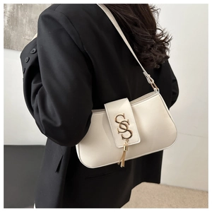 Detail of minimalist beige baguette bag with golden S logo and fringe on a black blazer
