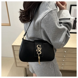 Detail of black faux leather underarm bag with gold S-buckle and elegant metal tassels