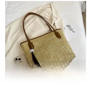 Close-up of woven straw tote bag with brown leather handles and decorative tassel