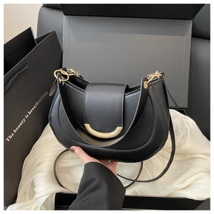 Close-up of black leather half-moon bag with gold buckle on white silk background