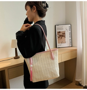 Detail of woven straw tote bag with pink leather strap and side fringe tassel decoration