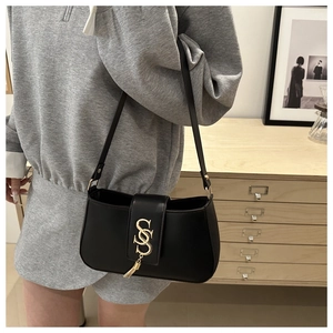 Close-up of black shoulder bag with golden S-shaped buckle and tassel on model