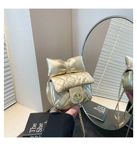 Detail of gold quilted mini crossbody bag with metal bow and chain strap in a mirror reflection