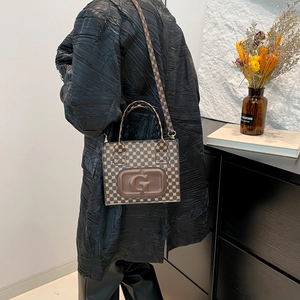 Brown vintage tote bag with embossed G logo and pattern worn as shoulder bag
