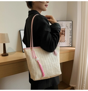 Detail of straw tote bag showing beige woven texture with pink leather trim and long tassel