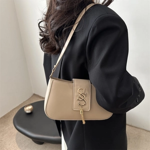 Chic beige half-moon underarm bag with gold S-logo and fringe detail on black blazer