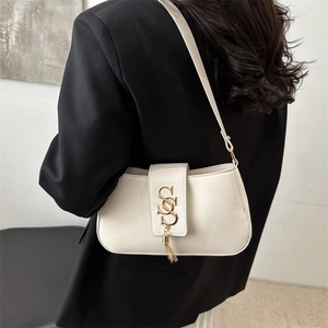 Chic off-white leather shoulder bag with gold S-buckle and tassel on a female model