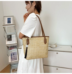 Detail of woven straw tote bag with brown leather handles and a fringe tassel