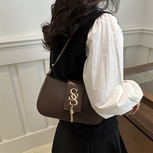 Minimalist dark brown leather baguette bag with golden logo and tassel worn by model
