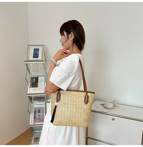 Close-up of a woven straw tote bag with brown leather handles and black tassel detail