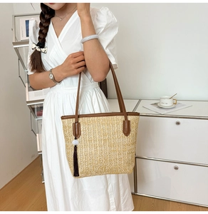 Detail of woven straw tote bag featuring brown leather straps and beaded tassel charm
