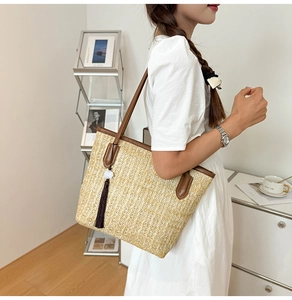 Detail of a beige straw tote bag featuring brown leather trim and stylish long tassels
