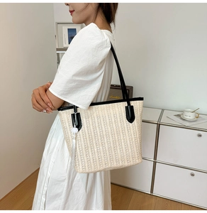 Detail of a large woven straw tote bag featuring black leather straps and white fringe tassel