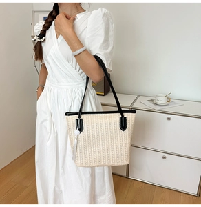 Detail of hand-woven straw tote bag with black leather straps and beaded tassel accent