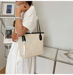 Fashionable woven straw tote bag with black leather straps on white dress model