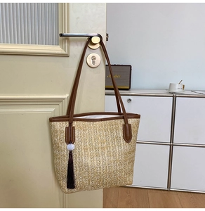 Close-up of woven straw tote bag featuring brown leather straps and long tassel detail