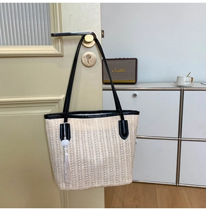 Detail of woven straw tote bag with black leather straps and white tassel on a door
