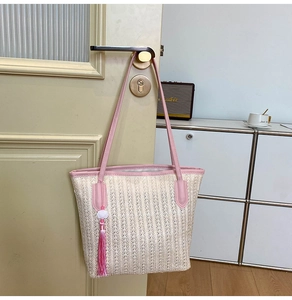 Detail of straw woven tote bag with pink tassels hanging on a light wooden door handle