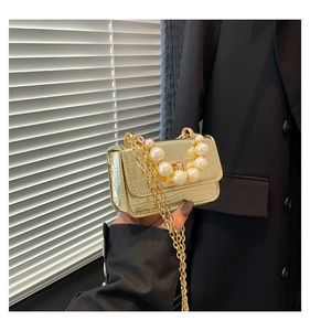 Detail of gold mini handbag with crocodile texture and elegant large pearl handle