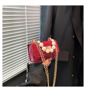 Macro detail of red crocodile texture mini bag with elegant pearl accents and gold chain