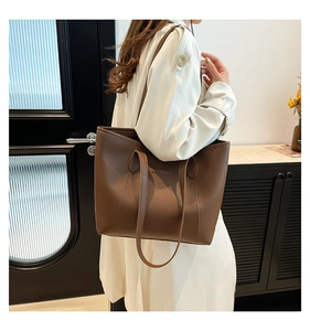 Détail du grand sac cabas en cuir marron avec logo embossé porté par le modèle