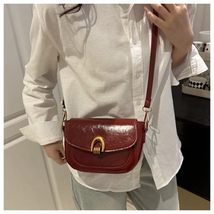Detail of burgundy patent leather saddle bag with distinctive gold U-shaped metal buckle