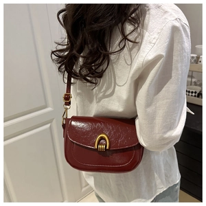 Close-up of wine red saddle bag with glossy wrinkled texture and golden horseshoe buckle