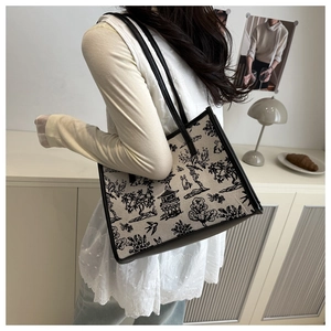 Detail of a beige canvas tote bag with black Toile de Jouy oriental pattern and leather handles