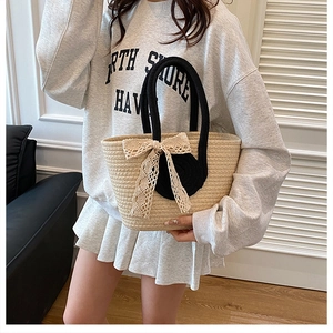 Détail du sac cabas en paille tissée avec poignées noires et grand nœud en dentelle