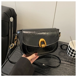 Detailed view of vintage black glossy saddle bag featuring a bold gold U-shaped metal buckle