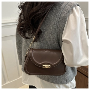 Close-up of a brown leather shoulder bag with a cylindrical gold buckle on a model