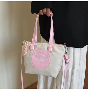 Détail d'un sac cabas beige et rose avec bandoulières en cuir et écusson rond brodé