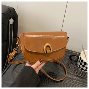 Detail view of brown vintage saddle bag featuring a gold horseshoe buckle and vegan leather
