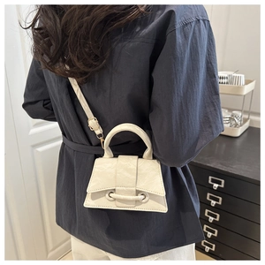 Detail of a beige textured mini trapezoid handbag worn crossbody on a navy shirt