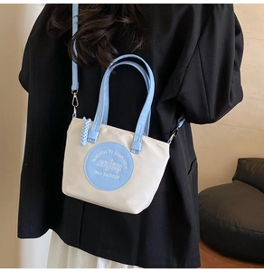 Détail du sac bandoulière en toile beige avec écusson bleu clair et anses assorties