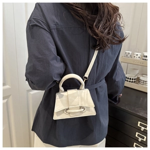 White mini trapezoid handbag with curved base and crossbody strap worn by a model