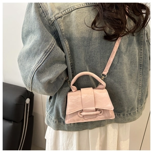 Detail of a structured pale pink crossbody bag styled with a vintage denim jacket
