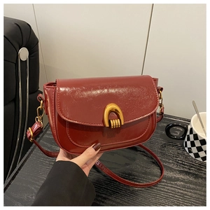 Detail of burgundy vintage saddle bag with glossy texture and gold horseshoe buckle