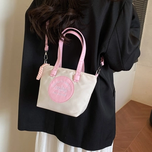 Sac fourre-tout tendance en nylon beige et rose porté en bandoulière sur un blazer