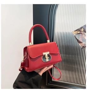 Detail of red leather handbag featuring unique gold T-bar buckle and cylindrical handle