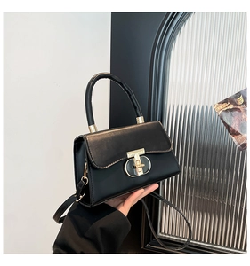 Detail of black leather handbag featuring a minimalist gold twist lock and a round handle