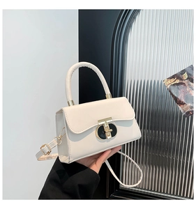 Detail of a creamy white leather handbag with a gold twist lock and adjustable shoulder strap
