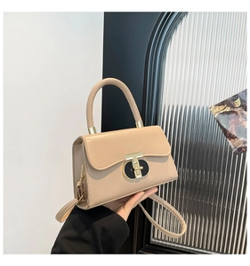 Detailed close-up of a beige leather handbag featuring a distinct golden T-shaped metal lock