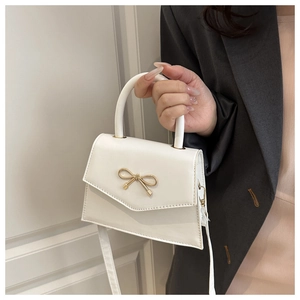 Detailed shot of white crossbody bag featuring a decorative golden bow metal clasp