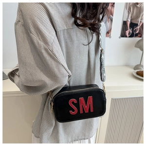 Detail der schwarzen Leder-Umhängetasche mit rotem SM-Patch und gestreiftem Trageriemen