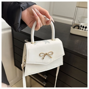 Close-up of a white mini handbag with a golden bow buckle and smooth faux leather texture