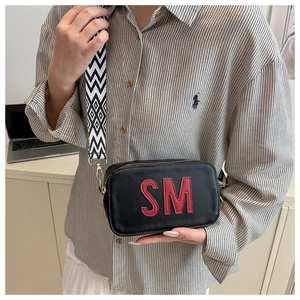 Details einer schwarzen Umhängetasche aus Leder mit SM-Buchstaben und Web-Gurt