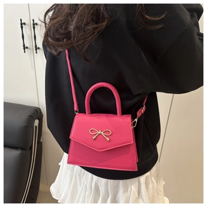 Rose pink mini handbag with gold bow charm shown worn by a model in a lifestyle setting