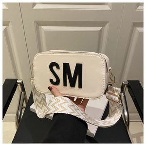 Detail der cremeweißen eckigen Tasche mit SM-Logo-Patch und gewebtem Schultergurt