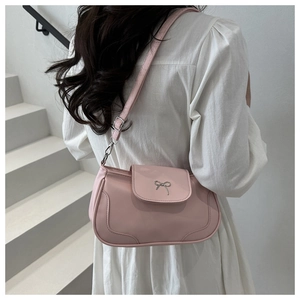 Détail d'un sac à bandoulière rose avec boucle nœud en métal argenté sur escalier